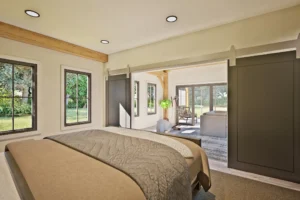 A cozy, light-colored bedroom looking out onto a living room. Ample window space illuminates the room, while open rolling barn doors allow for an open, accessible feel. The design is from the BigSkyHaven floor plan, the latest addition to the Woodhouse catalog.