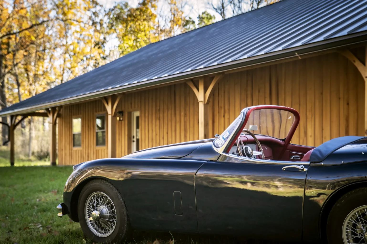 A classic car set in front of a timber frame car barn.