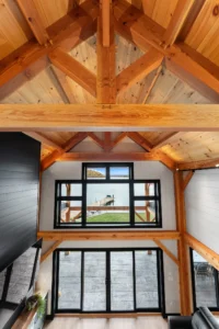 Vaulted timber frame ceiling with exposed trusses viewed from the loft, framing a large picture window with lake and dock views.