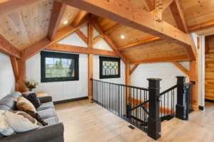 Cozy loft sitting area with timber frame beams, wood ceiling, black metal railing, and stained-glass accent window.