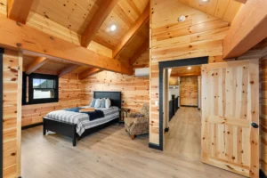 Timber frame bedroom with vaulted wood ceilings, exposed beams, natural wood walls, and a doorway leading to the upper-level hallway.