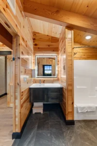 Wood-paneled bathroom with timber frame accents, modern vanity, illuminated mirror, and walk-in shower.