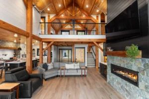 Expansive timber frame great room with vaulted ceilings, exposed beams, stone fireplace, and open loft overlooking the living space.
