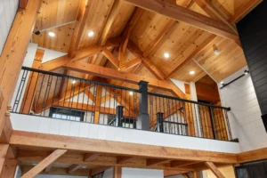 Upward view of the timber frame loft railing and vaulted ceiling showcasing exposed trusses and warm wood tones.