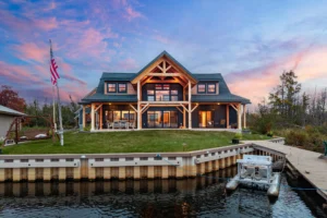 Wide sunset view of a timber frame lake house with dual covered patios, large sliding glass doors, and a private dock.