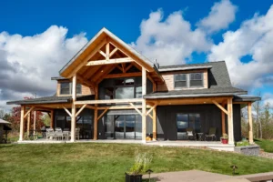 Two-story timber frame home with black and natural wood siding, large gabled porch, and expansive windows overlooking a lakeside property in Michigan’s Upper Peninsula.