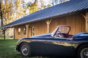 A classic car set in front of a timber frame car barn.