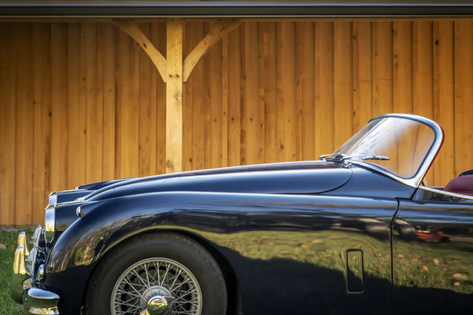 A classic car set in front of a timber frame car barn.