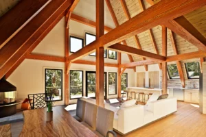 Open-concept interior of the AspenValley A-frame timber frame home featuring exposed wood beams, vaulted ceiling, large windows, modern kitchen, and living area filled with natural light.