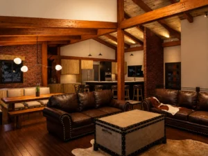 Open-concept contemporary timber frame great room with exposed beams, brick fireplace, modern kitchen, and vaulted ceilings.
