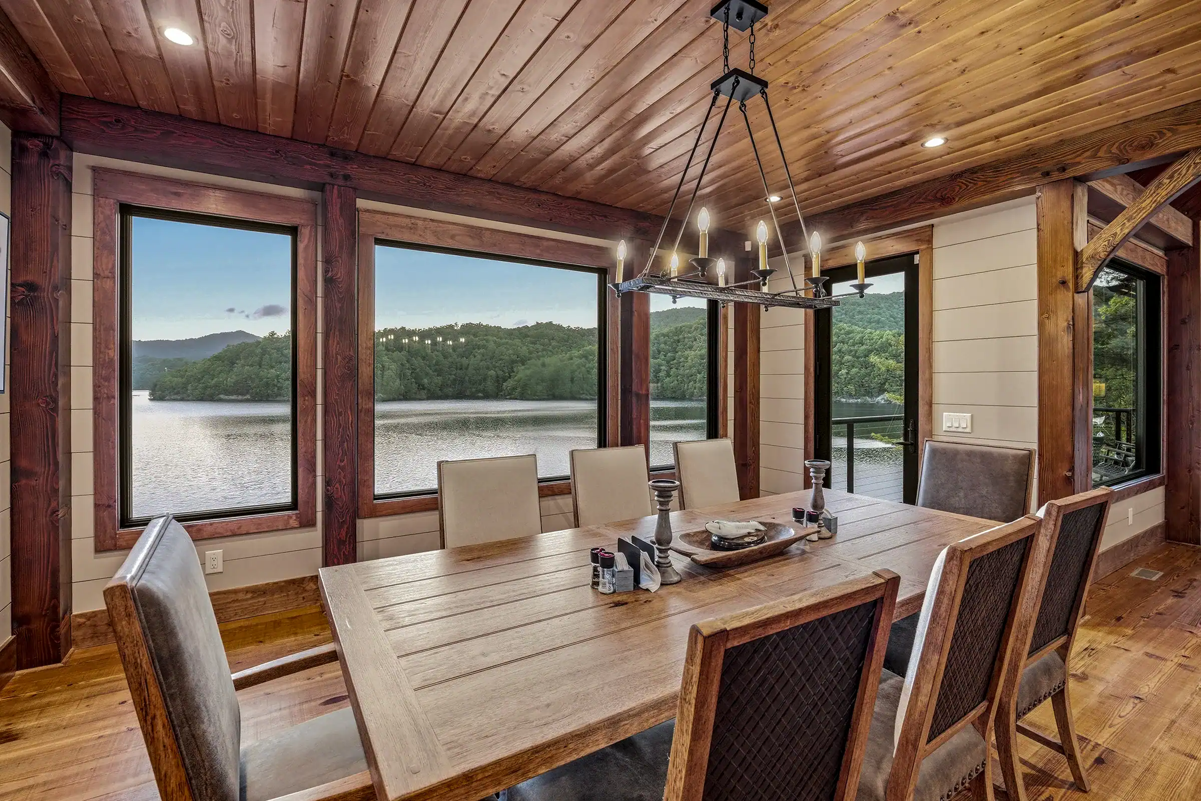 Luxury timber frame dining room with exposed wood beams, vaulted ceilings, and panoramic lake views through expansive windows.
