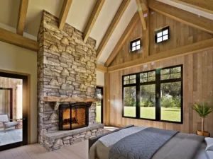 Primary bedroom with vaulted timber ceiling, floor-to-ceiling stone fireplace, large windows, and warm rustic finishes creating a luxury retreat atmosphere.