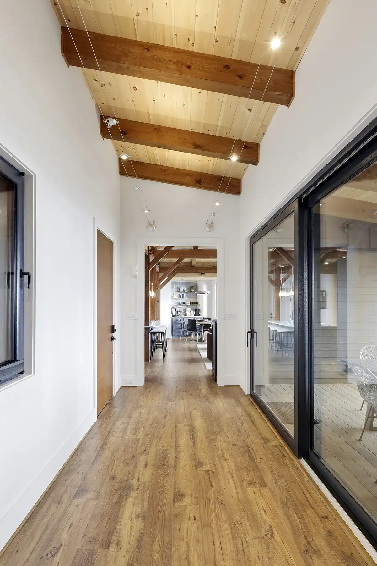 Interior hallway with exposed timber beams, wood ceiling, and large glass doors connecting the living spaces of a custom contemporary timber frame home on Snakeden Mountain.