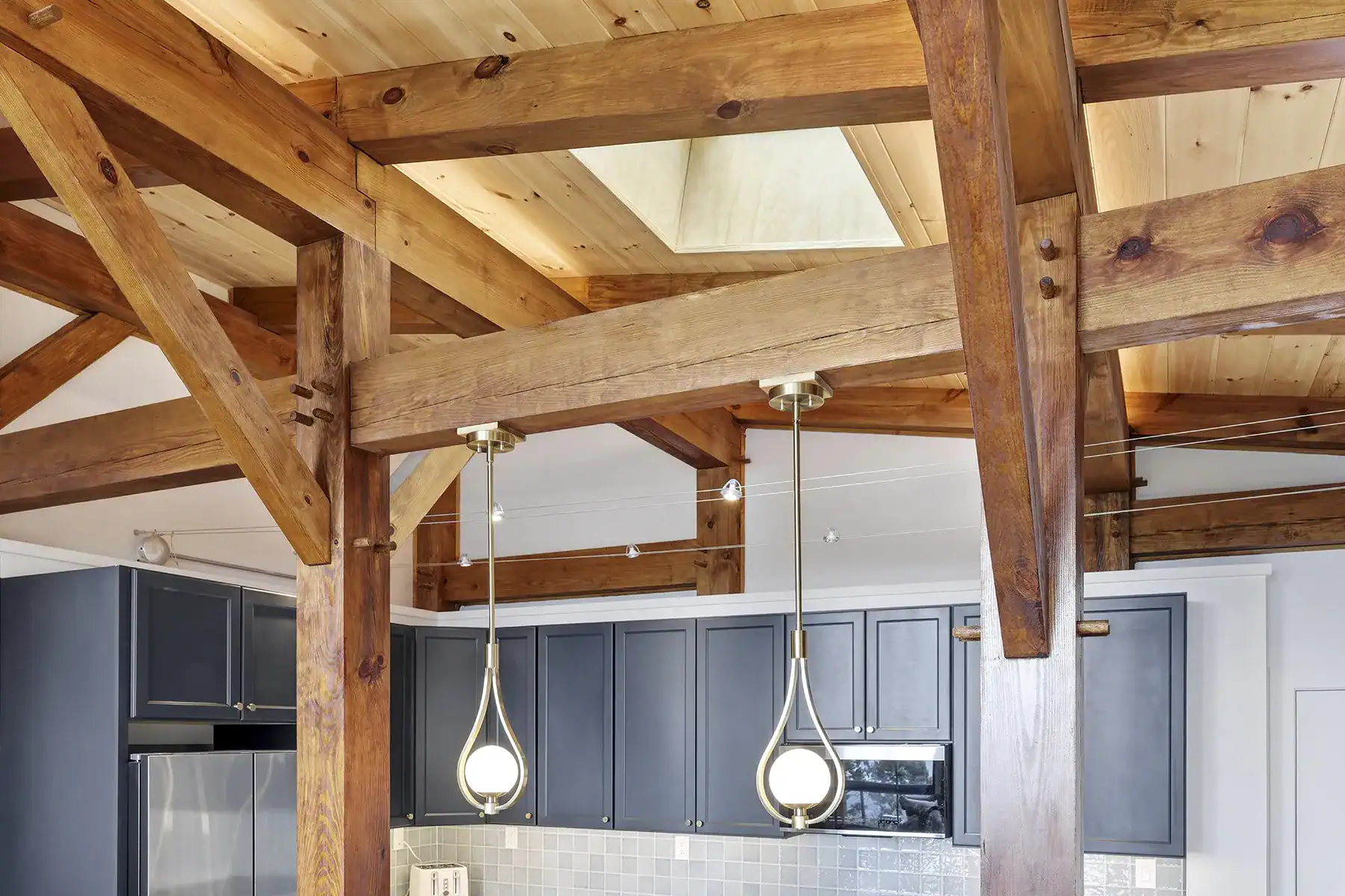 Exposed timber posts, beams, and knee braces frame a contemporary kitchen with pendant lighting in a custom timber frame home on Snakeden Mountain.