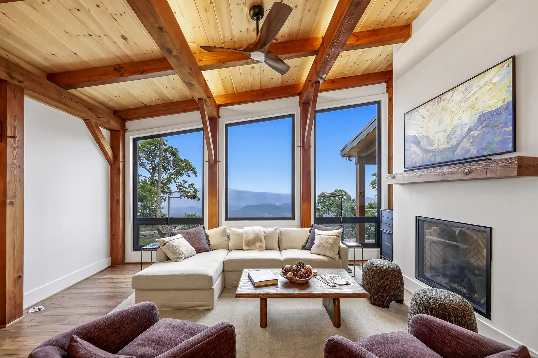 Great room with exposed timber framing, fireplace, and floor-to-ceiling windows overlooking the mountains in a custom contemporary timber frame home on Snakeden Mountain.