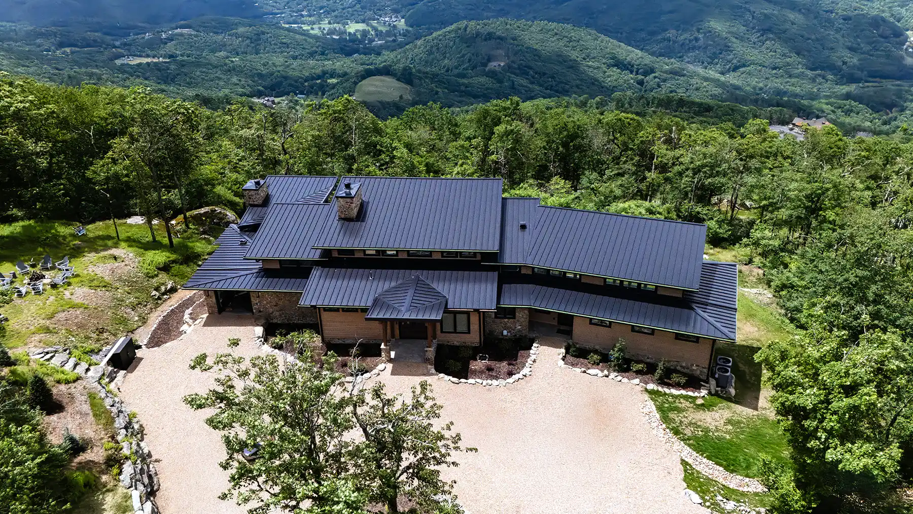 Aerial view of a timber frame mountain home surrounded by forest with sweeping Blue Ridge Mountain views near Banner Elk, North Carolina.