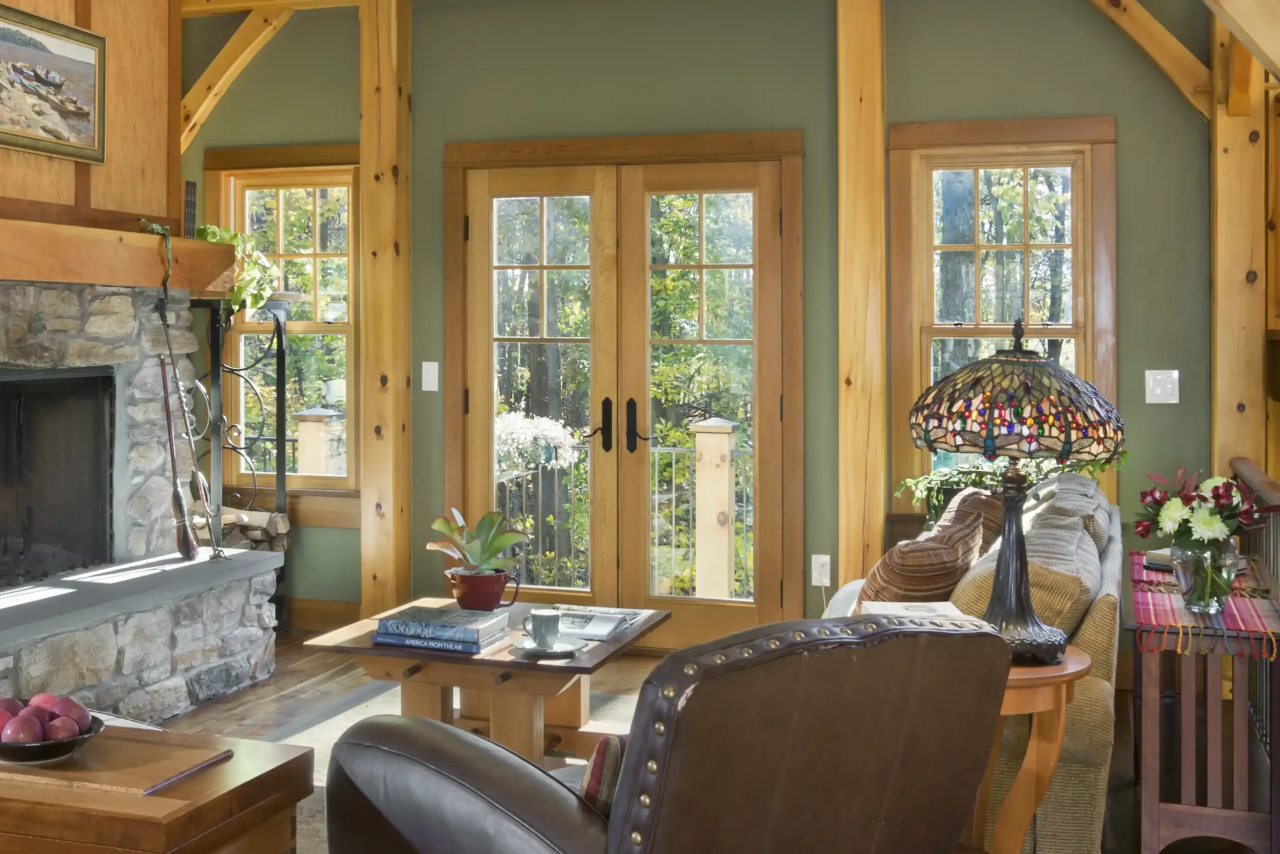 French doors with divided-light glass open from a timber frame living room, flanked by windows and framed by exposed wood posts and beams.