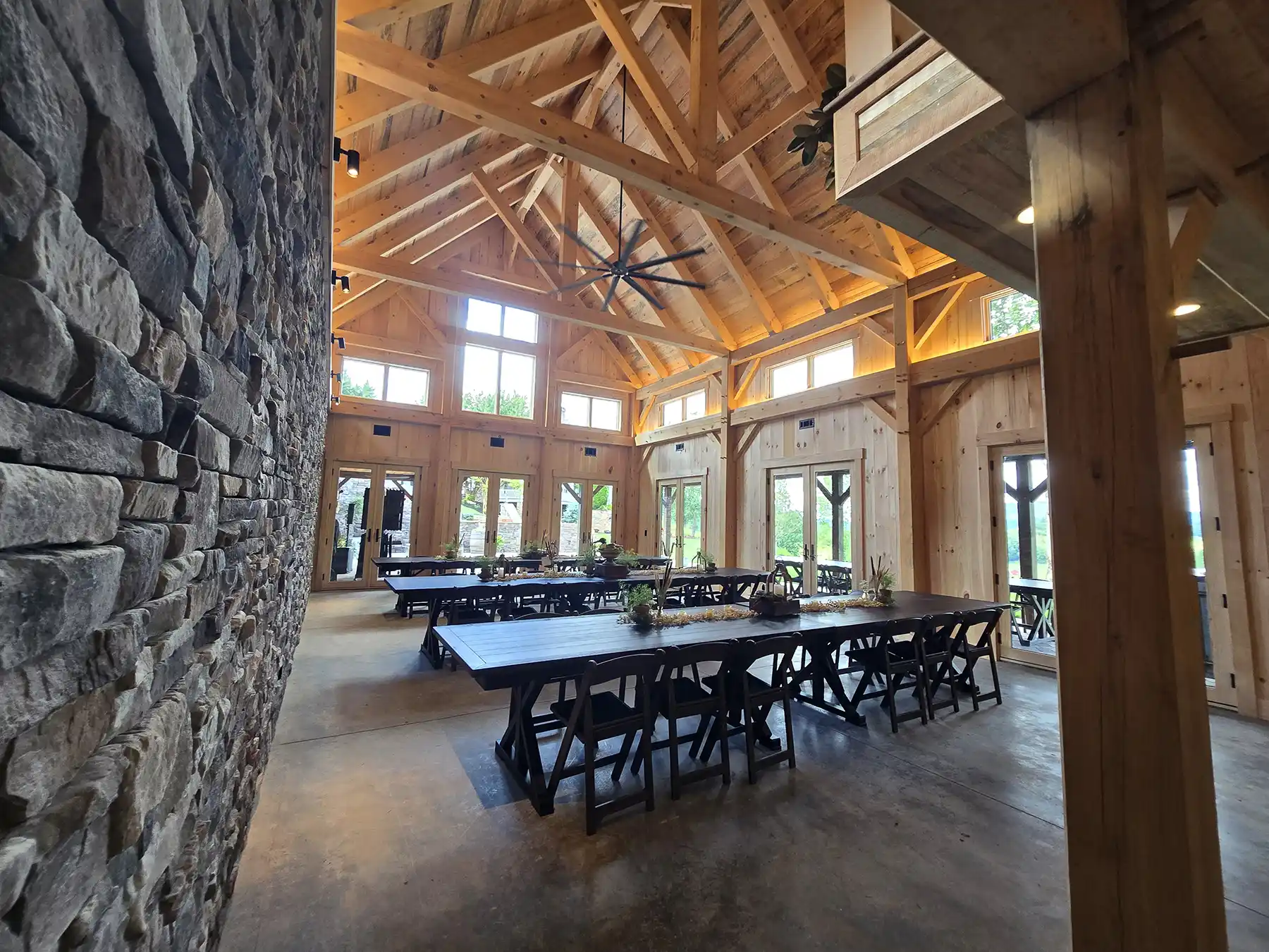 Interior view of the Oak & Vine Event Center showing exposed timber framing, vaulted ceilings, large windows, stonework, and event seating.