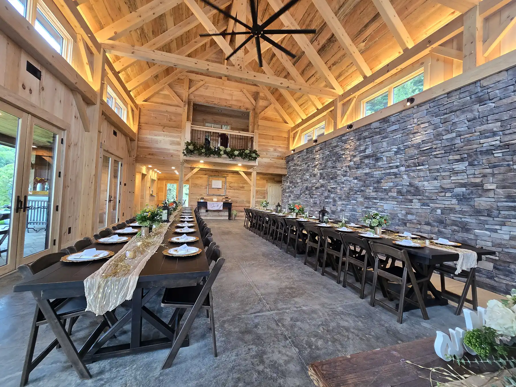 Interior of the Oak & Vine Event Center featuring exposed eastern white pine timber framing, king post trusses, stonework, and long dining tables set for an event.