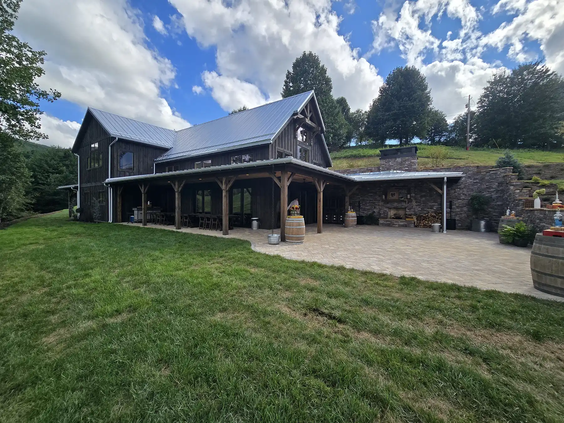 Exterior of the Oak & Vine Event Center showing the dark wood siding, metal roof, covered white oak porch, stone patio, and outdoor fireplace.