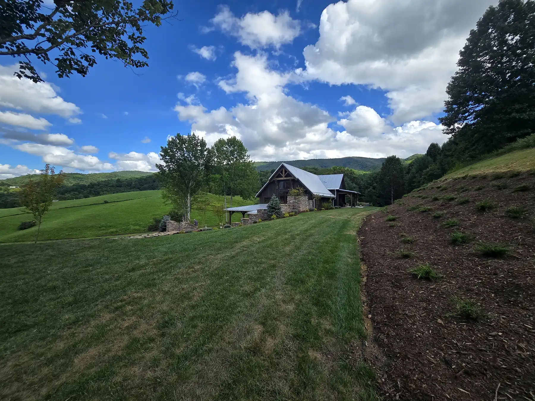 Wide view of Oak & Vine Farms in Mountain City, Tennessee, with the timber frame event center set against rolling green hills and mountain views.