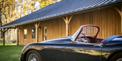A classic car set in front of a timber frame car barn.