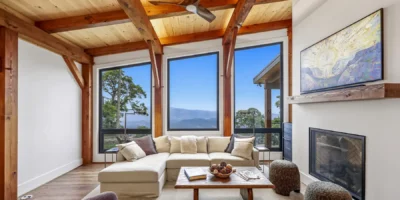 Great room with exposed timber framing, fireplace, and floor-to-ceiling windows overlooking the mountains in a custom contemporary timber frame home on Snakeden Mountain.