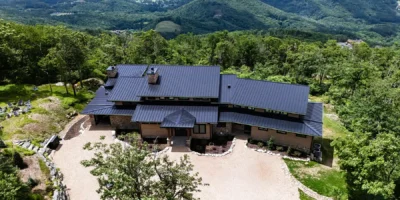 Aerial view of a timber frame mountain home surrounded by forest with sweeping Blue Ridge Mountain views near Banner Elk, North Carolina.